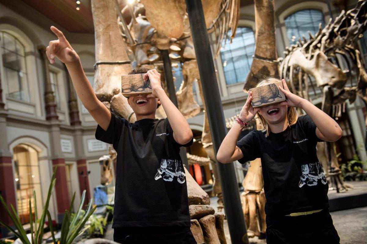Zwei Kinder mit Google Cardboard Brillen unter dem Giraffatitan brancai