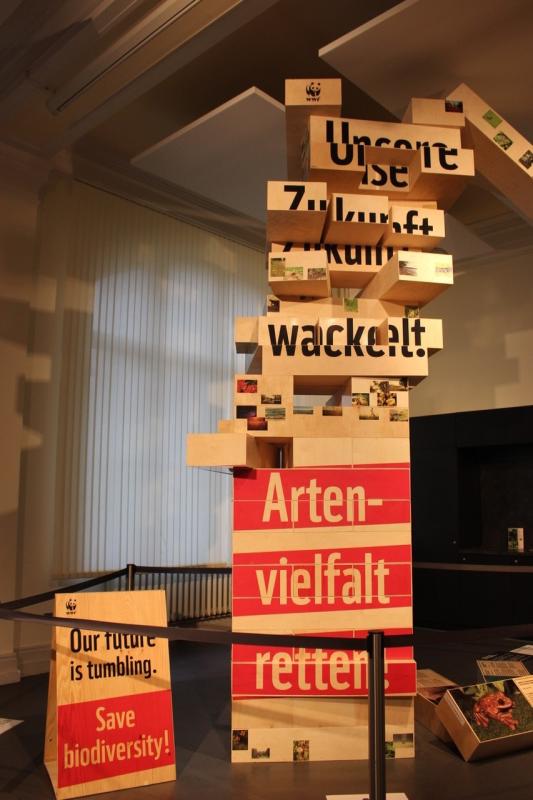 Ein vier Meter hoher Turm aus Klötzen addressiert die Arten- und Biodiversitätskrise. Dort wo einige Blöcke fehlen gerät der Turm ins Wanken. Ein vier Meter hoher Turm aus Klötzen addressiert die Arten- und Biodiversitätskrise. Dort wo einige Blöcke fehlen gerät der Turm ins Wanken.