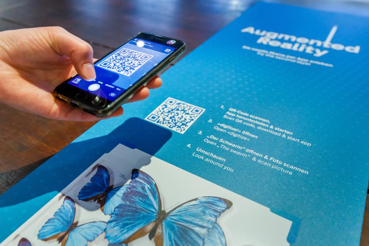 Person scannt mit Smartphone einen QR Code in der Ausstellung