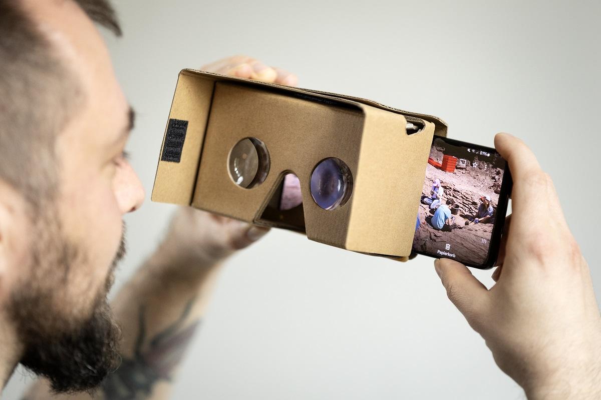 Steffen Bock holding cardboard 360-degree virtual reality glasses with a smartphone inserted behind their lenses.