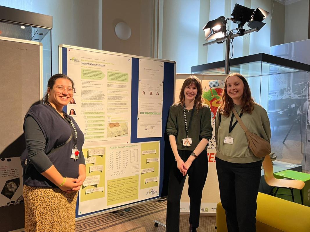 Sarah Ziehn (studentische Mitarbeitende), Saskia Brunst (Koordinatorin) und Hanna Wüste (studentische Mitarbeitende) beim Stand der Transkriptionswerkstatt. Quelle: Privat