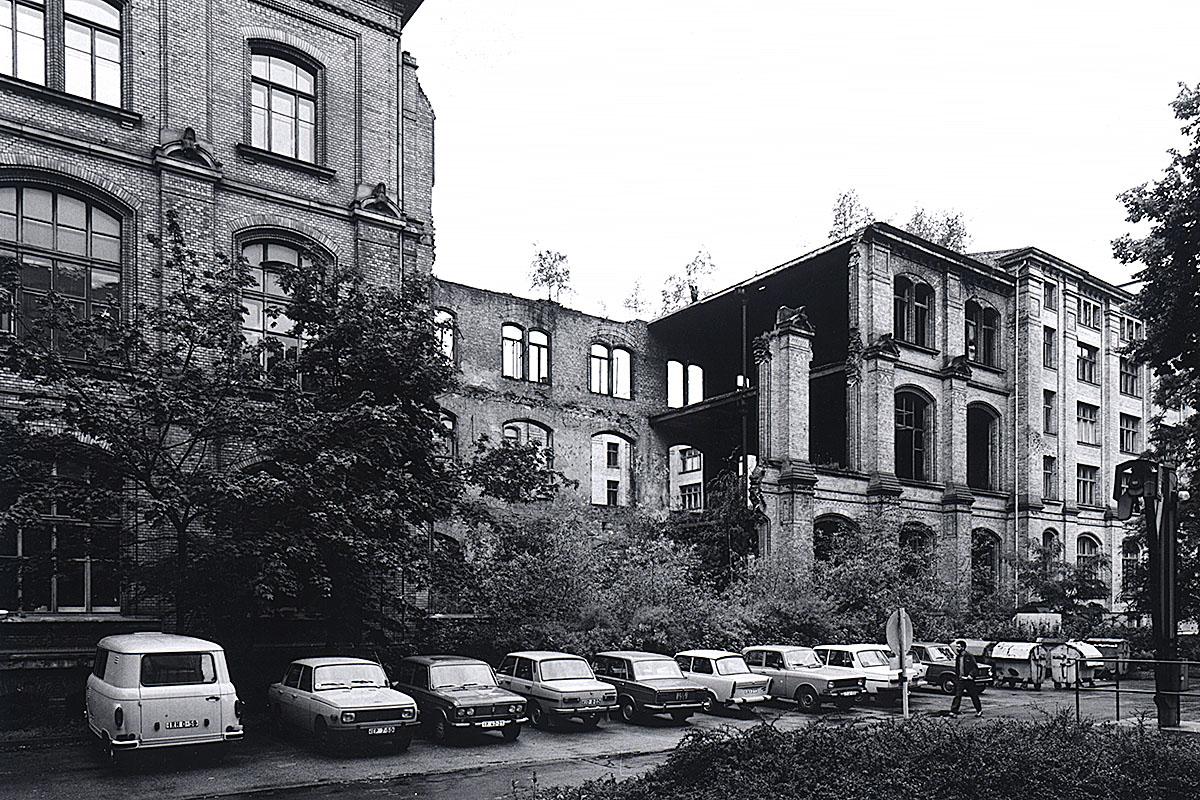 Das Foto zeigt den zerstörten Ostflügel des Gebäudes mit davor parkenden Autos. 