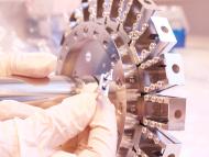 Nahaufnahme von Probenrevolver und Glühdraht eines Massenspektrometers im Labor; eine Person mit Handschuhen hält diese fest. 