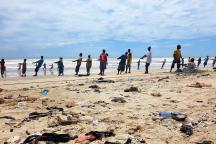Fischer an einem Strand an der Atlantikküste Ghanas, davor zu sehen viel Plastikmüll im Sand.