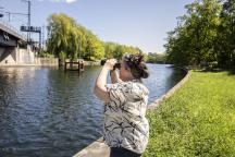 Eine Ehrenamtliche beobachtet mit einem Fernglas Vögel am Fluss Panke in Berlin